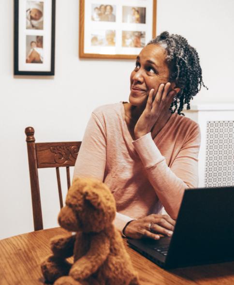 Woman sitting at table with laptop looking up and smiling at someone out of frame